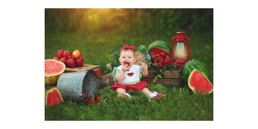عکاسی کودک شب یلدا در طبیعت با دکور میوه های قرمز و سبز